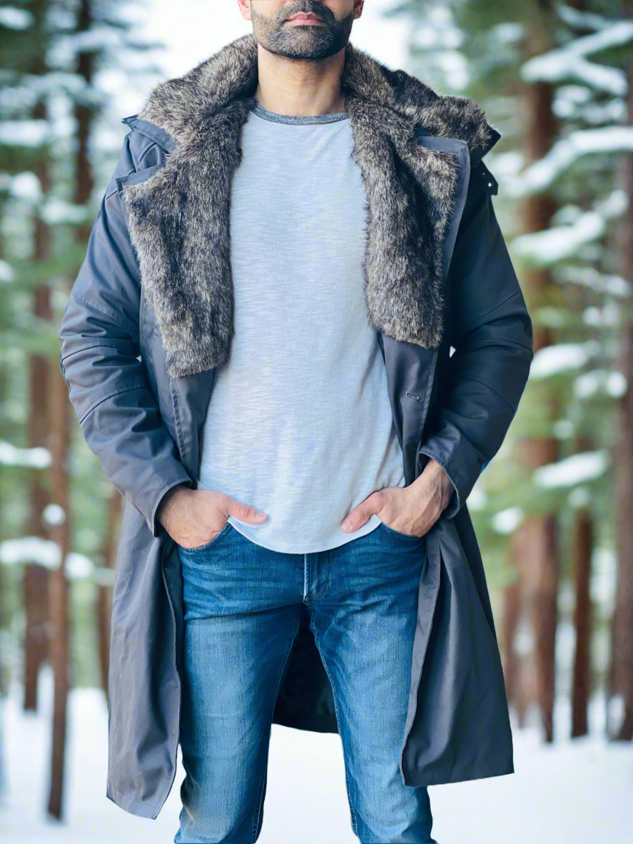 Man wearing a long dark coat with a fur-lined hood in a snowy forest setting