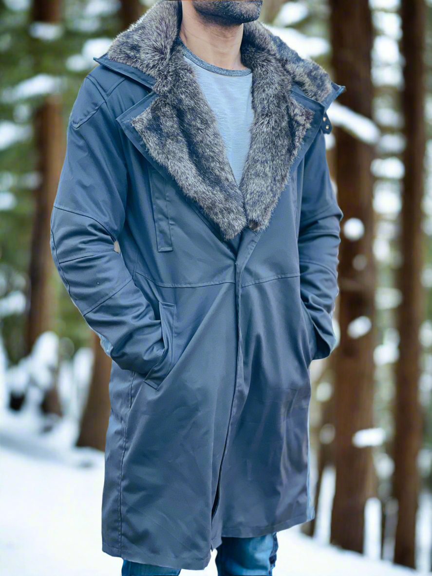 Person wearing a long blue coat with gray fur collar in a snowy forest setting